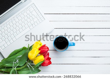 Cup of coffee and tulips with notebook on white wooden background.