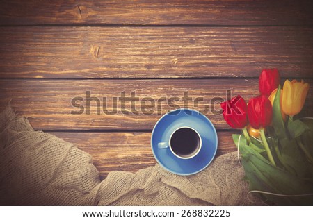 Cup of coffee with tulips near fabric on wooden table. Photo in old color image style.