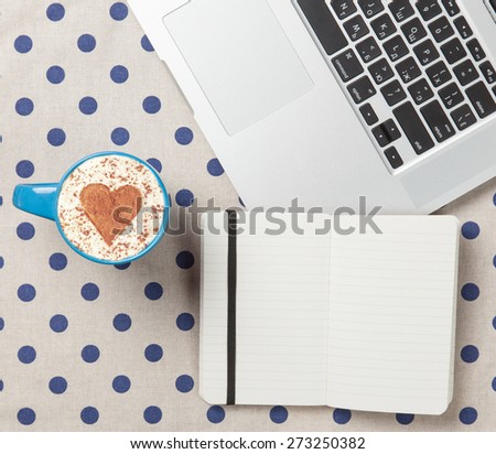 Cup of cappuccino with heart shape and laptop with note on polka dot background.