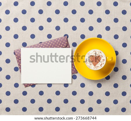 Cup of cappuccino with heart shape and envelope on polka dot background.
