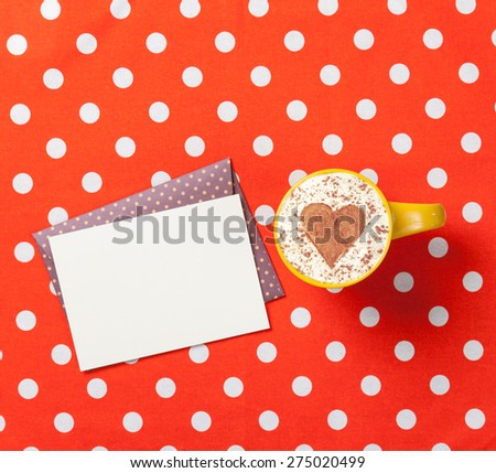 Cup of cappuccino with heart shape and envelope with gift box on red polka dot background.