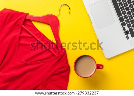 Cup of coffee and laptop computer near red dress on yellow background