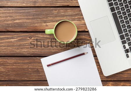 Cup of coffee and paper with laptop computer on wooden background