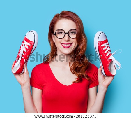 Smiling redhead girl in red dress with gumshoes on yellow background.