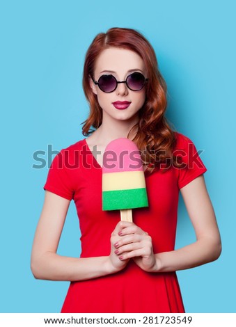 Young redhead student girl in red dress with toy ice-cream on blue background.