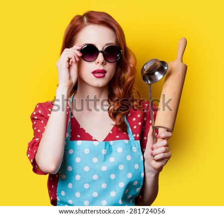 Surprised redhead girl in red polka dot dress with plunger on yellow background.