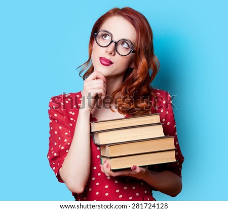 Young redhead teacher in red polka dot dress with books on blue background.