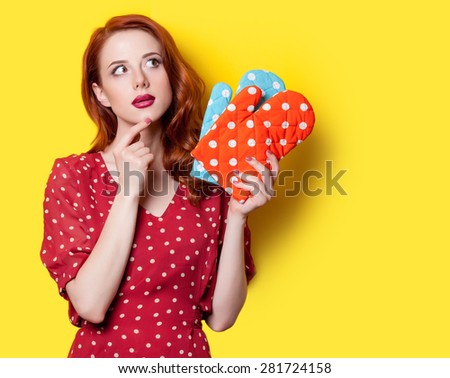 Surprised redhead girl in red polka dot dress and mittens on yellow background.