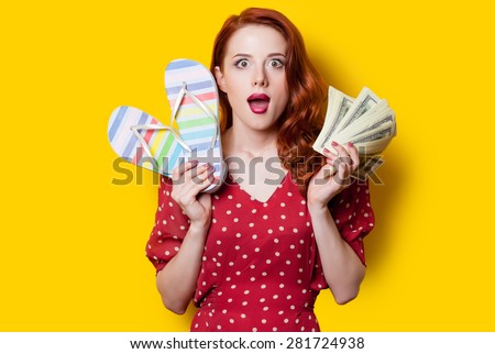 Surprised redhead girl in red polka dot dress with flip flops and money on yellow background.