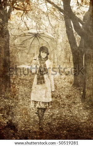 Girl in cloak and scarf with umbrella at park in rainy day. Photo in old image style.