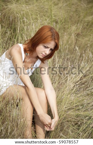 Sad red-haired girl at grass. Outdoor photo.