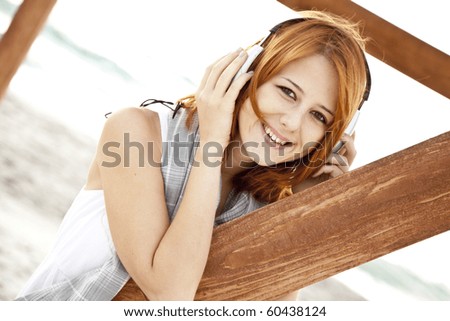 Portrait of young red-haired girl in headphone near wood at beach.