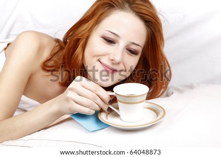 Pretty red-haired sleeping woman in white nightie lying in the bed near cup of coffee and reading note.