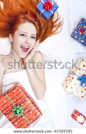 Happy red-haired girl in bed with Christmas gifts. Studio shot.