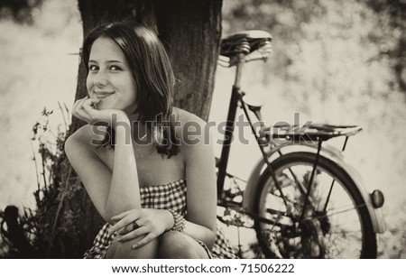 Beautiful girl sitting near bike and tree at rest in forest. Photo in old colour image style.