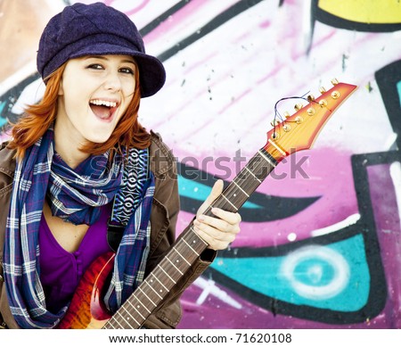 Closeup portrait of a happy young girl with guitar and graffiti on background