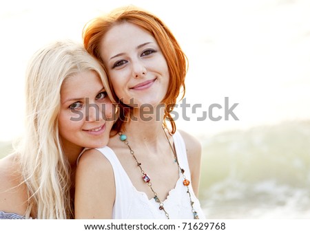 Two beautiful young girlfriends in hat on the beach at sunset. Photo with counter-light on background.