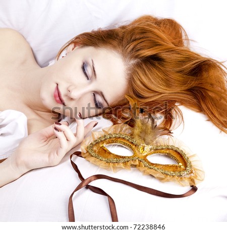 Pretty red-haired sleeping woman in white lying in the bed near carnival mask.