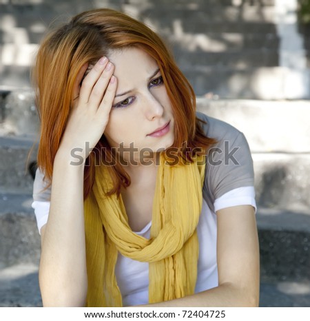 Sad red-haired girl at garden. Outdoor photo.