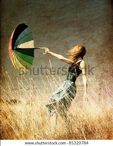 Redhead girl with umbrella at windy grass meadow. Photo in old color image style.