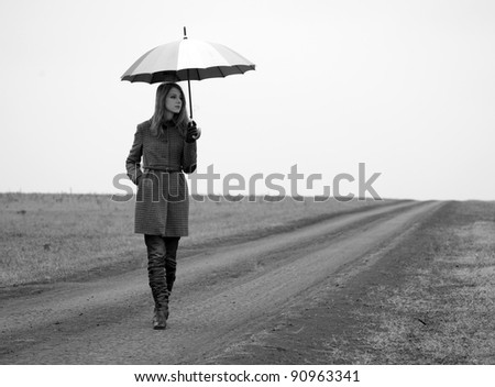 Lonely girl with umbrella at country road. Photo in old black and white style with little noise.