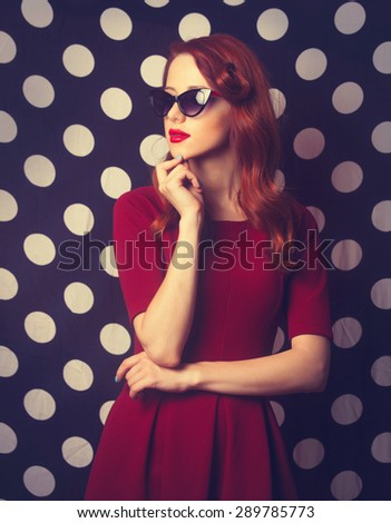 Portrait of a beautiful redhead girl in red dress on black and white polka dot background