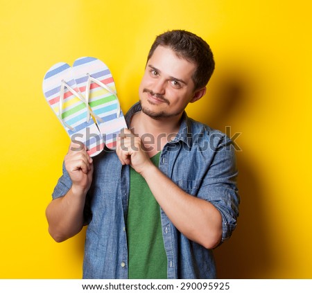young smiling guy in shirt with flip flops on yellow background.