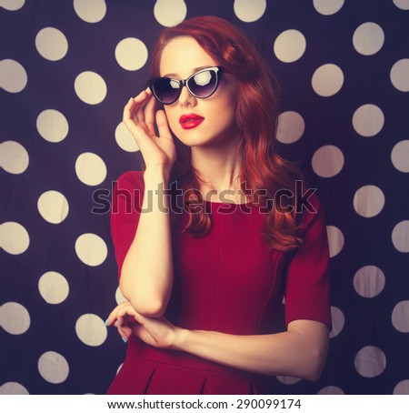 Portrait of a beautiful redhead girl in red dress on black and white polka dot background