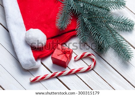 Santas hat and christmas candy with brench and red gift on white wooden table.