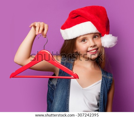 Beautiful young girl in red Santas hat with hanger on violet background.