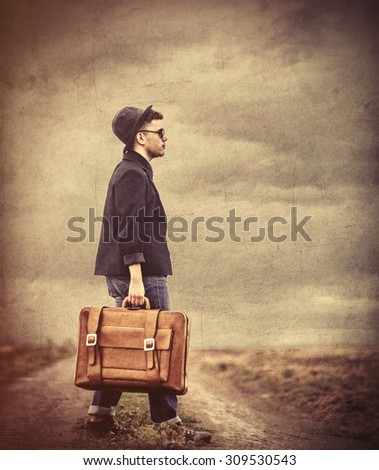 Style young man with suitcase at countryside outdoor. Photo in old color image style.