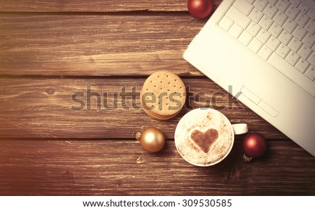 Cup of coffee with heart shape and laptop computer on wooden table.