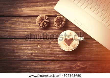 Cup of coffee with heart shape and laptop computer on wooden table.