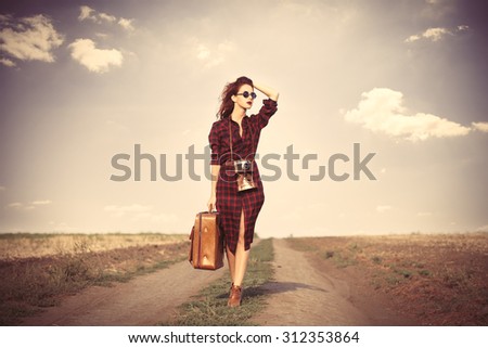 Beautiful girl in plaid dress with bag and retro camera on countryside