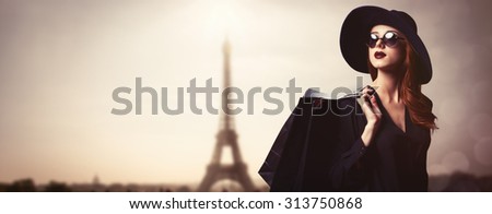 Style redhead girl with sunglasses and shopping bags on Eiffel tower background.