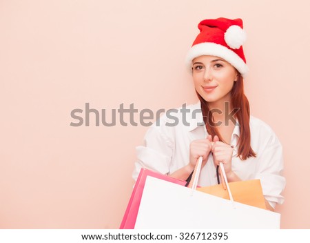 Portrait of a smiling redhead woman with shopping bags in Santa Claus hat on pink background