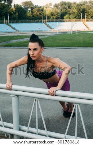 Slim athletic woman with dumbbells in the stadium. Sporty sexy girl with flat belly workout, outdoors