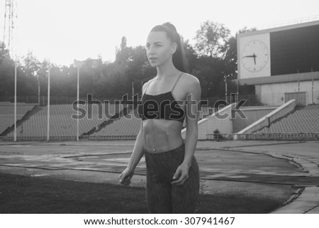 Slim athletic woman with dumbbells in the stadium. Sporty sexy girl with flat belly workout, outdoors