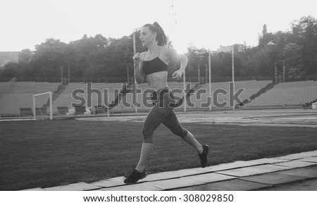 Slim athletic woman with dumbbells in the stadium. Sporty sexy girl with flat belly workout, outdoors
