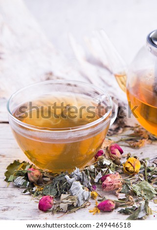 Transparent teapot of herbal tea with hot mug and dry roses on the tree white bark