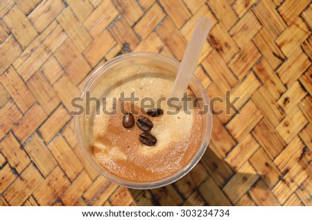 Glass of coffee frappe with rich foam and coffee beans on wooden background