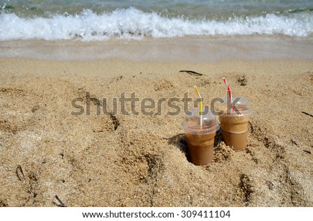 Cold coffee frappes set on beach with a wave in background