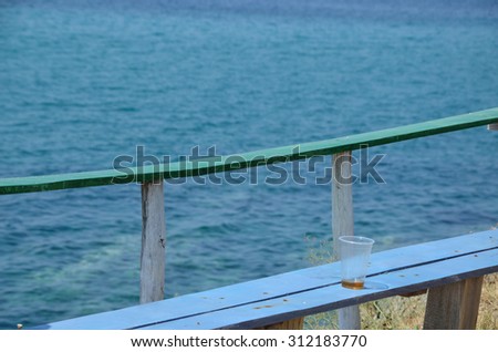 Empty plastic glass left on bar bench and bar table with sea in background