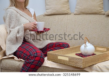 Lady in cozy home wear sitting on sofa and drinking tea