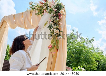 Decorating arch with textiles with flowers and plants. Woman organizer, owner, with digital tablet near wedding arch Stock fotó © 