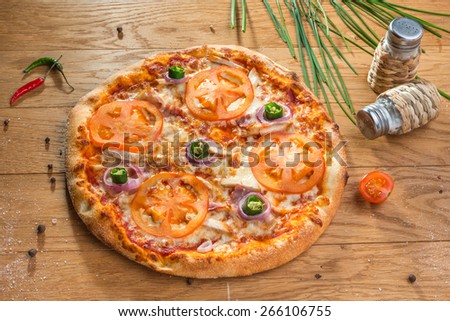 Delicious hot pizza with meet, tomatoes, onion and different spices on wooden table ready to eat