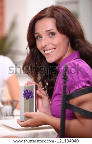 woman in restaurant with fiance smiling at camera with present