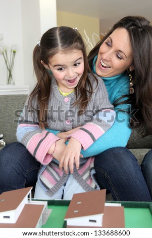 happy mother and young daughter looking at house model