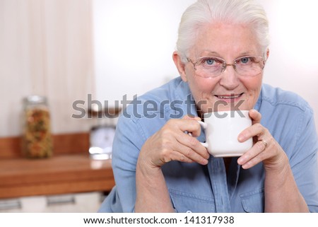 Elderly lady enjoying cup of tea in her kitchen