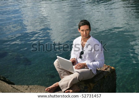 Man with laptop computer next to the sea